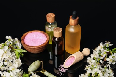 Photo of Spa composition with cosmetic products and beautiful flowers on black mirror surface, closeup