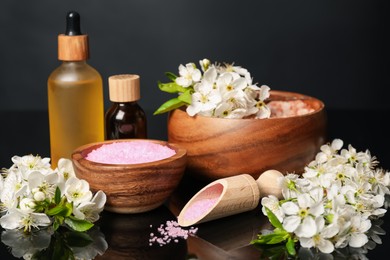 Photo of Spa composition with cosmetic products and beautiful flowers on black mirror surface, closeup
