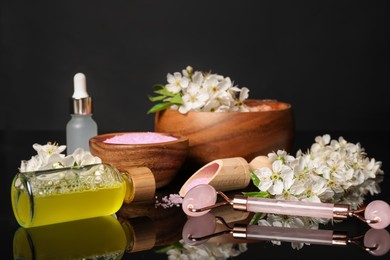 Photo of Spa composition with cosmetic products and beautiful flowers on black mirror surface, closeup