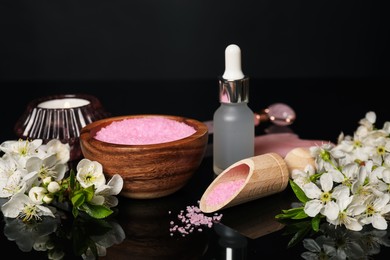 Photo of Spa composition with cosmetic products, burning candle and beautiful flowers on black mirror surface, closeup