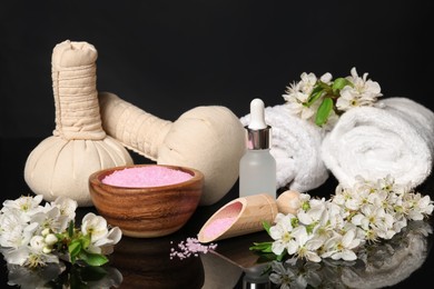 Photo of Spa composition with cosmetic products and beautiful flowers on black mirror surface, closeup