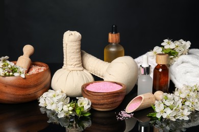 Photo of Spa composition with cosmetic products and beautiful flowers on black mirror surface, closeup