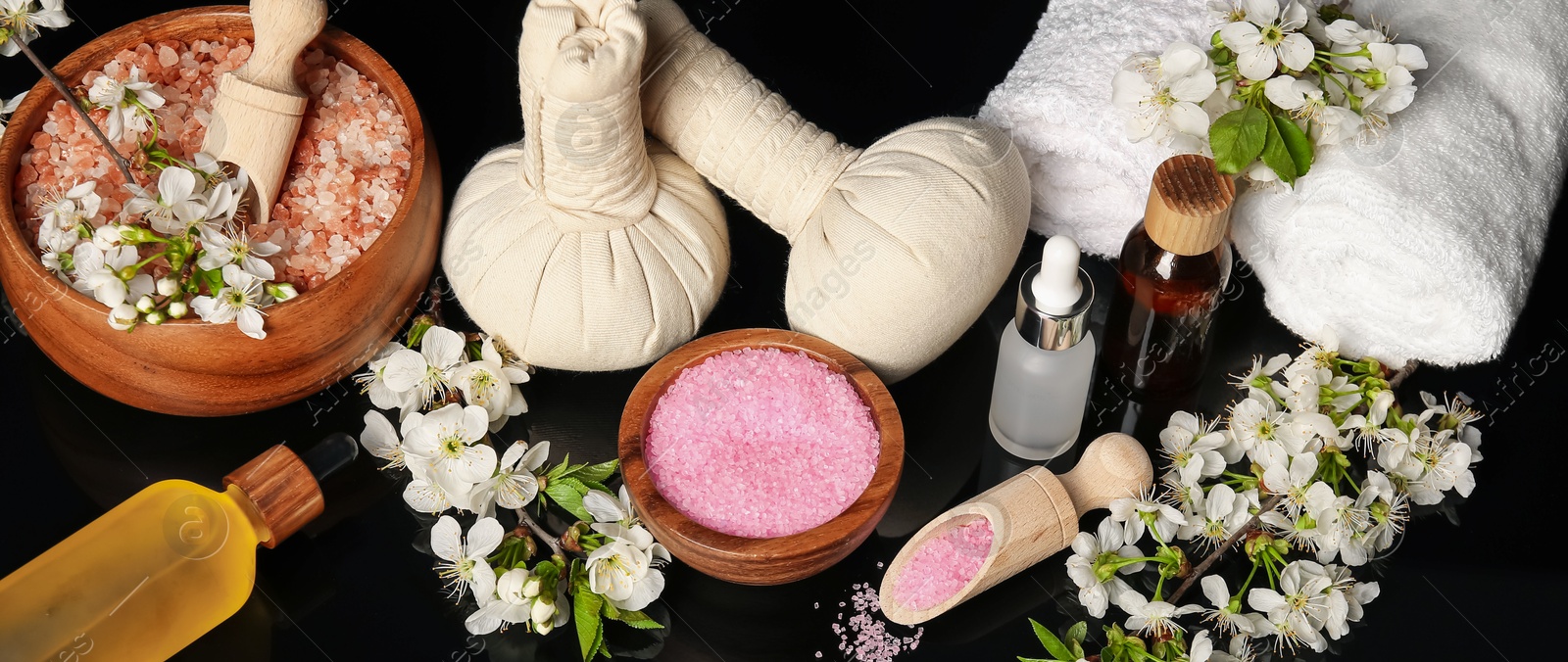 Spa composition with cosmetic products and beautiful flowers on black mirror surface Photo of Spa composition with cosmetic products and beautiful flowers on black mirror surface