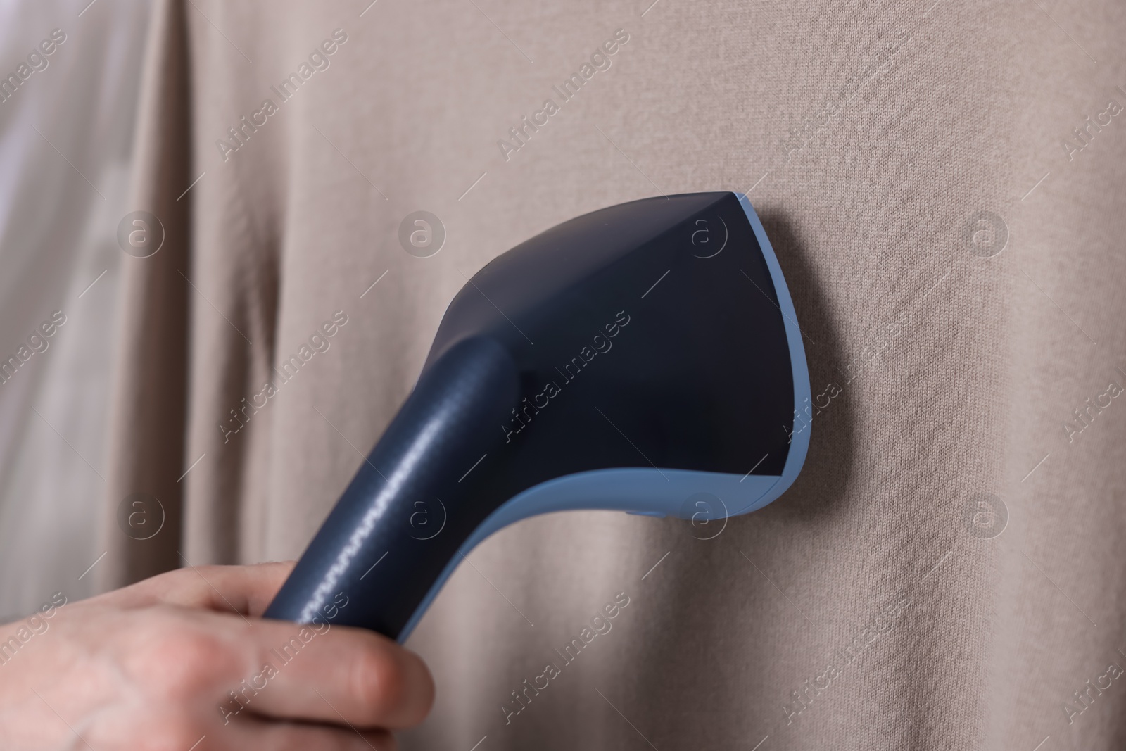 Photo of Man steaming shirt with stand steamer indoors, closeup