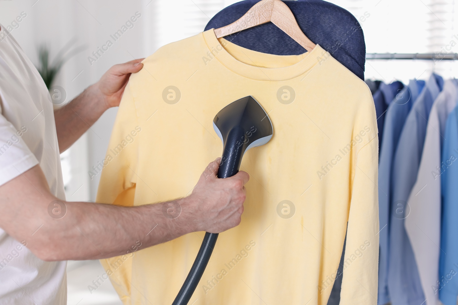 Photo of Man steaming shirt with stand steamer indoors, closeup