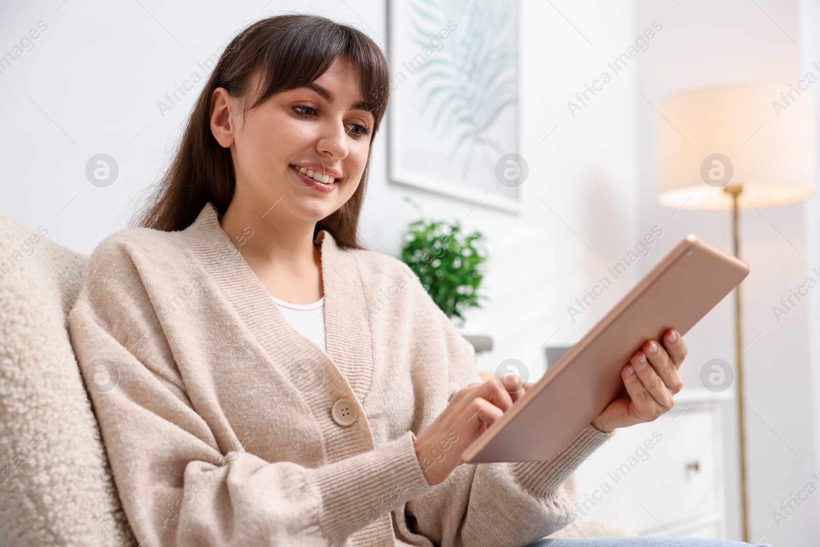 Woman using modern tablet in armchair at home. Space for text Photo of Woman using modern tablet in armchair at home. Space for text