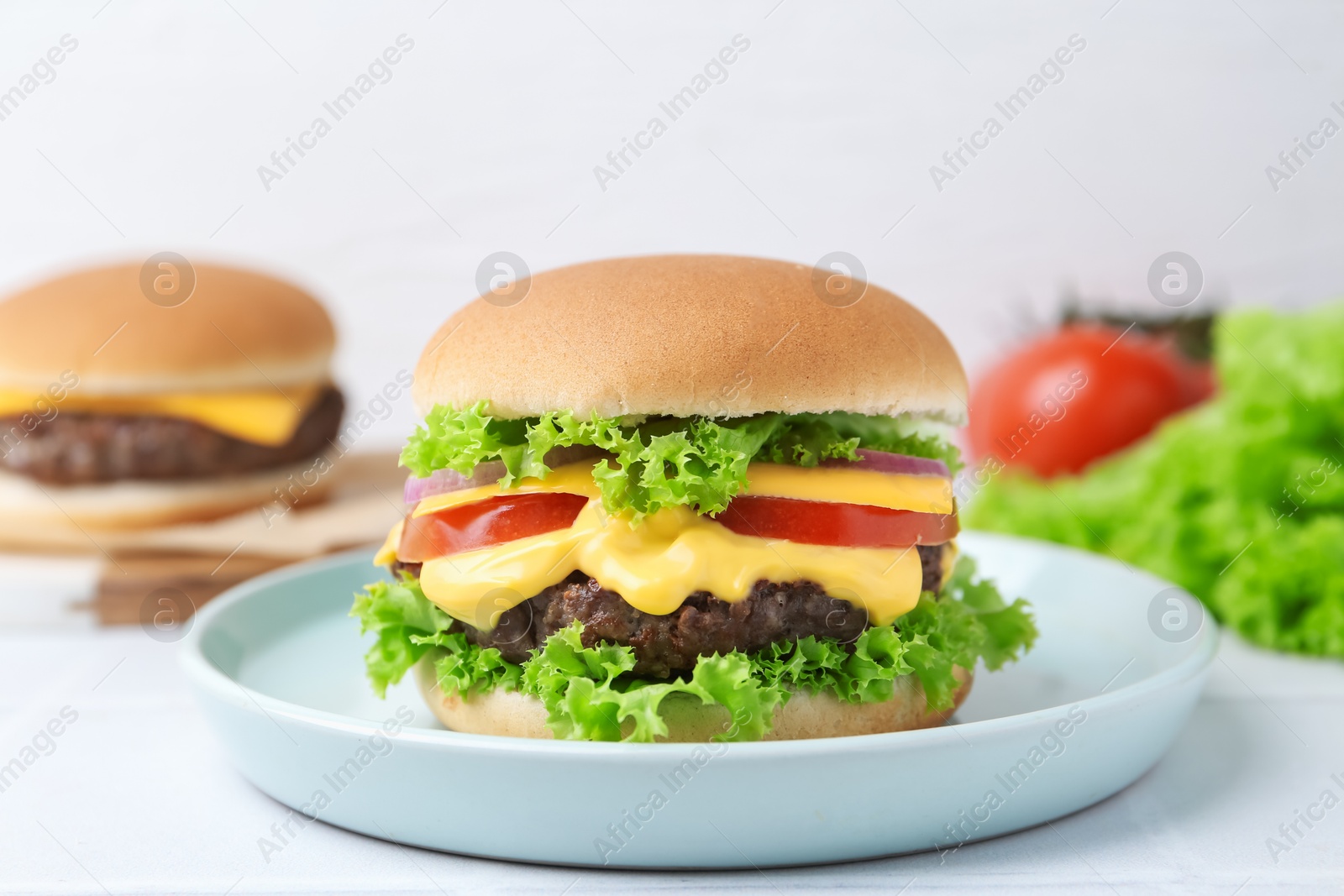 Tasty cheeseburger with lettuce and tomatoes on white table, closeup Photo of Tasty cheeseburger with lettuce and tomatoes on white table, closeup