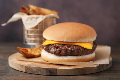 Photo of Tasty cheeseburger with potato wedges on wooden table, closeup