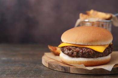 Photo of Tasty cheeseburger with potato wedges on wooden table, closeup. Space for text
