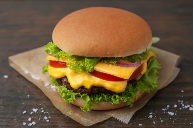 Photo of Tasty cheeseburger with lettuce and tomatoes on wooden table, closeup