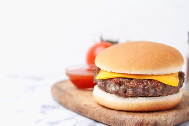 Photo of Tasty cheeseburger on white marble table, closeup. Space for text