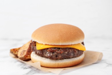 Photo of Tasty cheeseburger with potato wedges on white marble table, closeup
