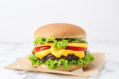 Photo of Tasty cheeseburger on white marble table, closeup