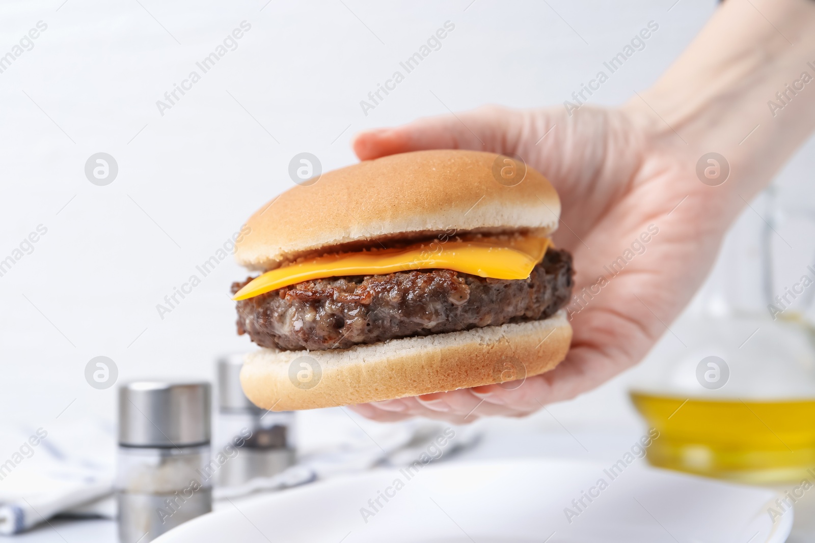 Woman holding tasty cheeseburger at white table, closeup Photo of Woman holding tasty cheeseburger at white table, closeup
