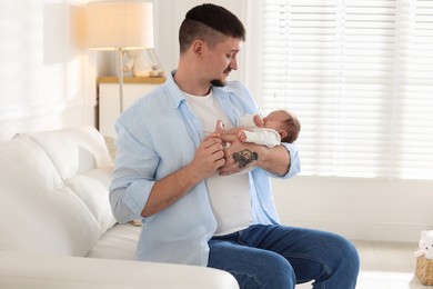 Photo of Father with his cute newborn baby on sofa indoors