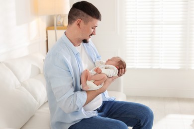 Photo of Father with his cute newborn baby on sofa indoors