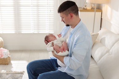 Photo of Father with his cute newborn baby on sofa indoors