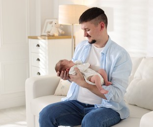 Photo of Father with his cute newborn baby on sofa indoors