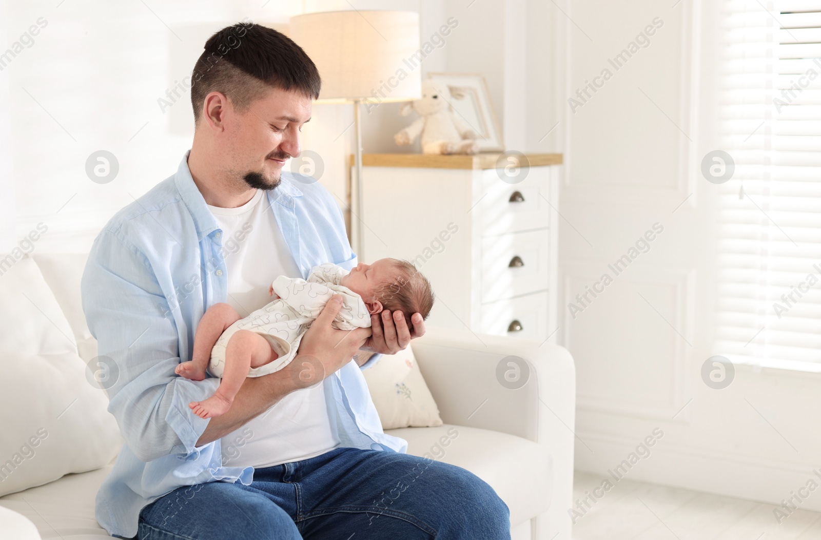 Photo of Father with his cute newborn baby on sofa indoors, space for text