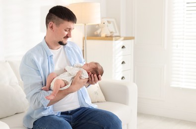 Photo of Father with his cute newborn baby on sofa indoors, space for text
