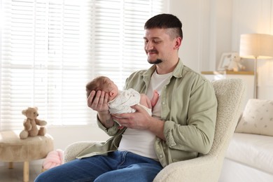 Photo of Father with his cute newborn baby in armchair indoors