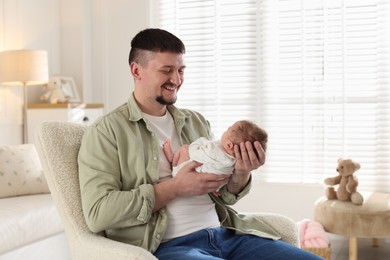 Photo of Father with his cute newborn baby in armchair indoors