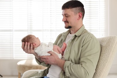 Photo of Father with his cute newborn baby in armchair indoors