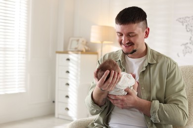 Photo of Father with his cute newborn baby in armchair indoors, space for text