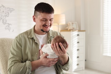 Photo of Father with his cute newborn baby in armchair indoors, space for text
