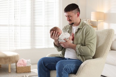 Photo of Father with his cute newborn baby in armchair indoors, space for text
