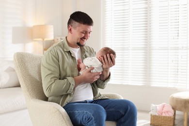 Photo of Father with his cute newborn baby in armchair indoors, space for text