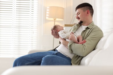 Photo of Father with his cute newborn baby on sofa indoors