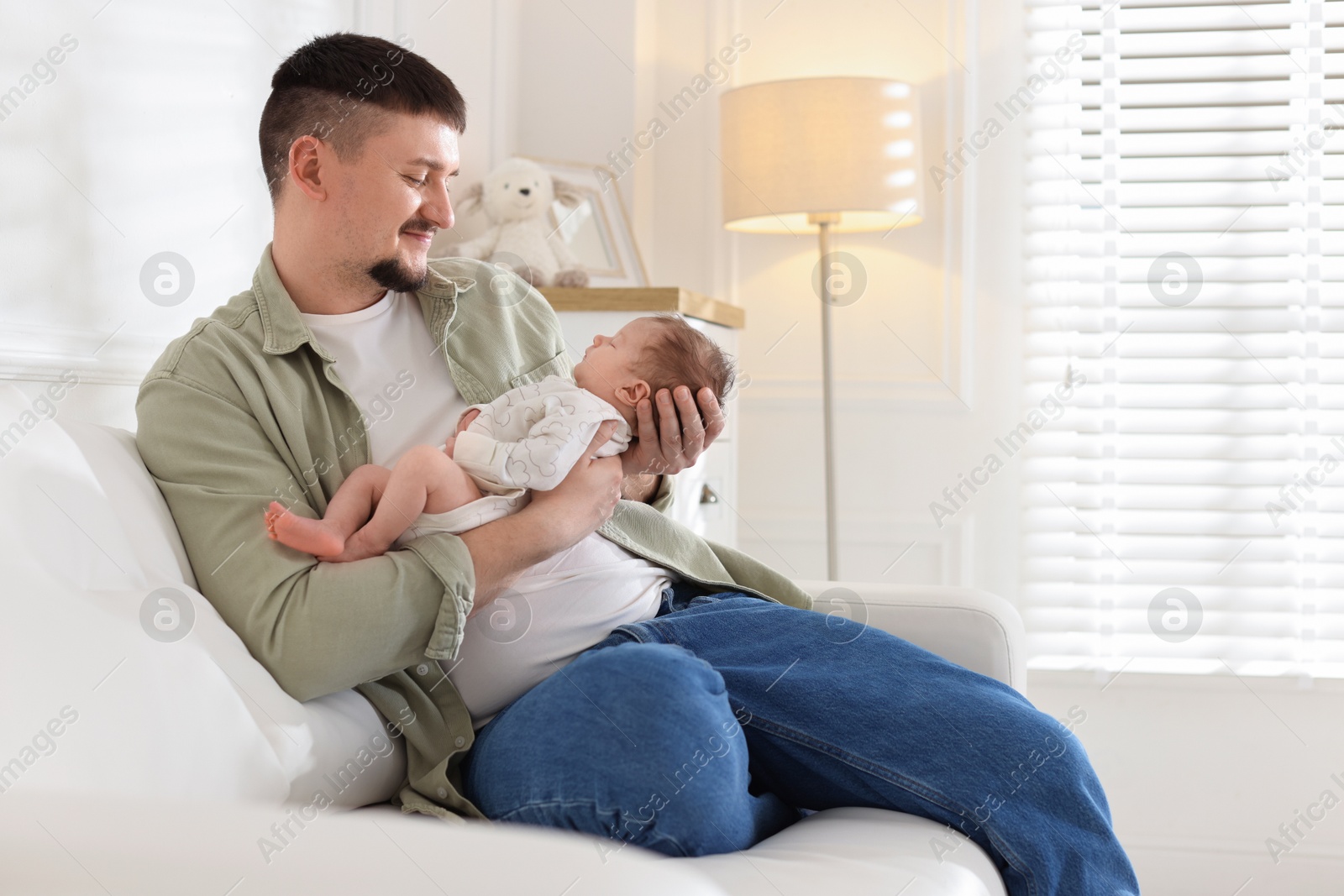 Father with his cute newborn baby on sofa indoors Photo of Father with his cute newborn baby on sofa indoors