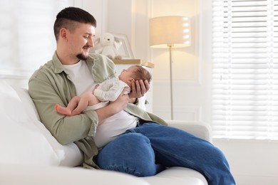 Photo of Father with his cute newborn baby on sofa indoors