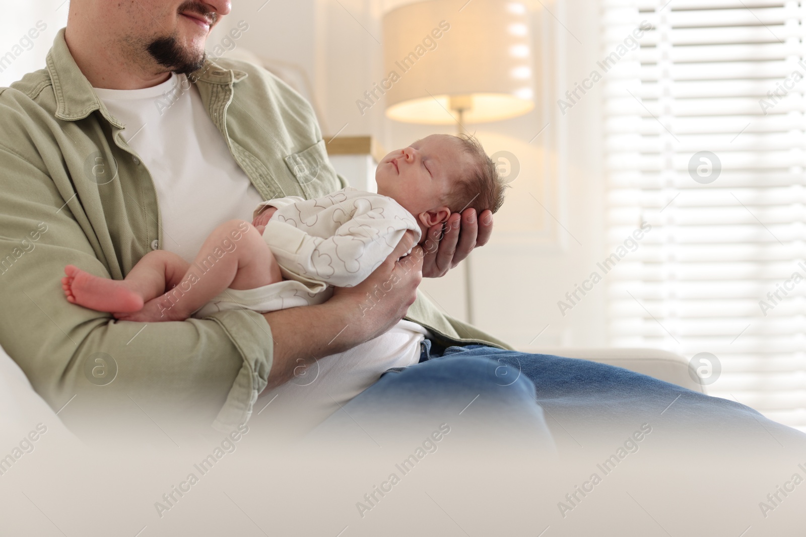 Photo of Father with his cute newborn baby on sofa indoors, closeup. Space for text