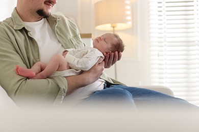 Photo of Father with his cute newborn baby on sofa indoors, closeup. Space for text