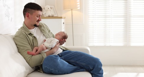 Photo of Father with his cute newborn baby on sofa indoors, space for text