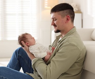 Photo of Father with his cute newborn baby near sofa indoors