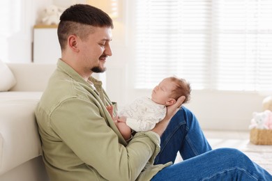 Photo of Father with his cute newborn baby near sofa indoors