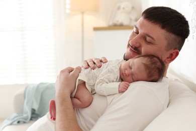 Photo of Father with his cute newborn baby on sofa indoors