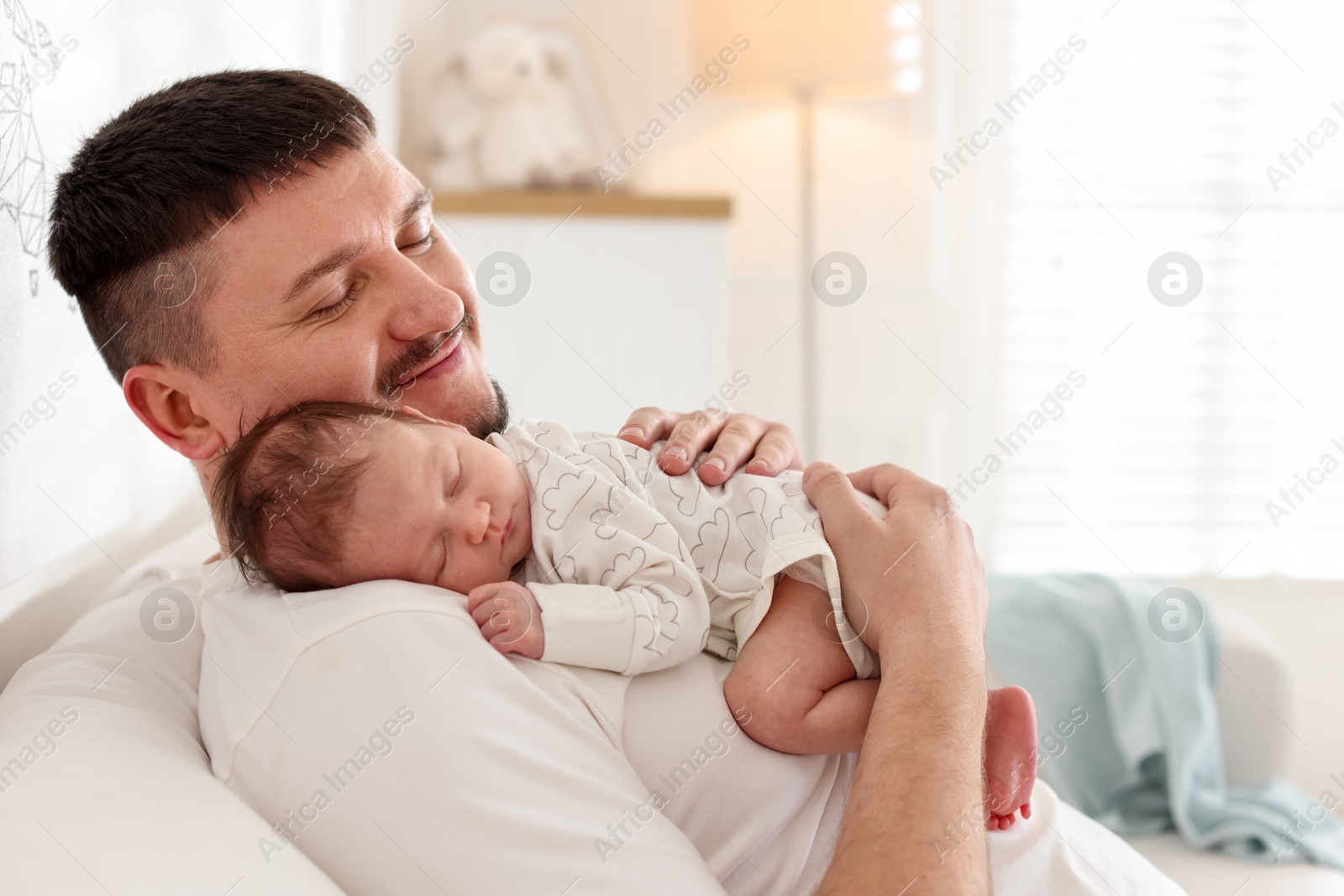 Photo of Father with his cute newborn baby on sofa indoors