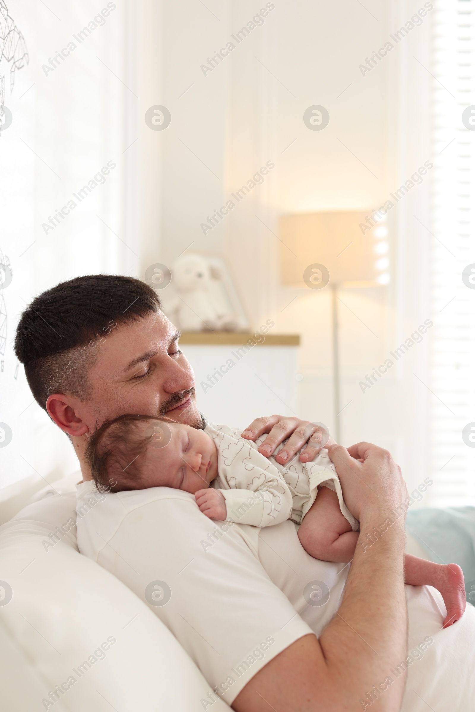 Photo of Father with his cute newborn baby on sofa indoors