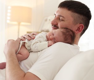 Photo of Father with his cute newborn baby on sofa indoors