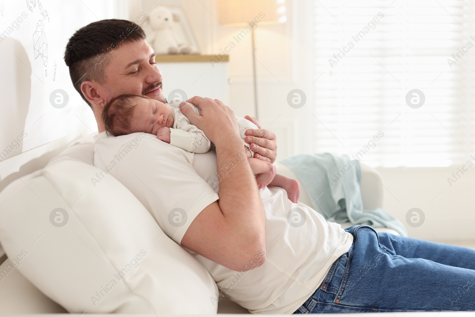 Photo of Father with his cute newborn baby on sofa indoors