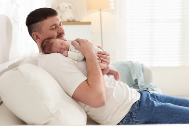 Photo of Father with his cute newborn baby on sofa indoors