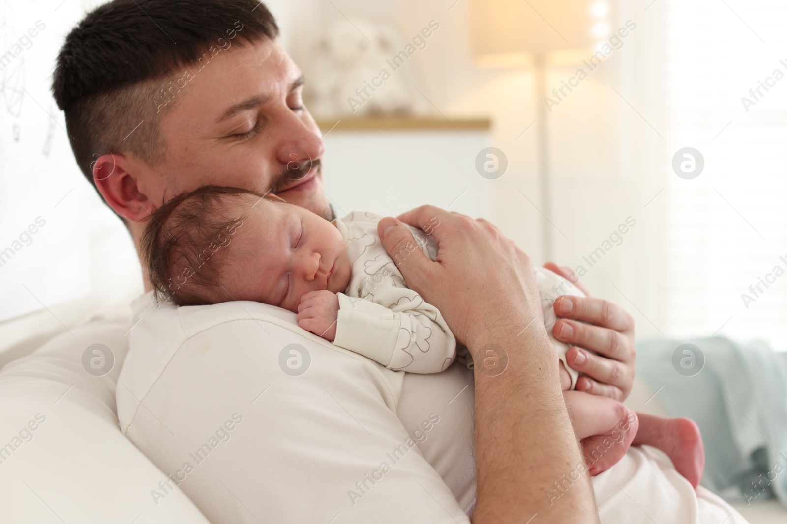 Photo of Father with his cute newborn baby on sofa indoors