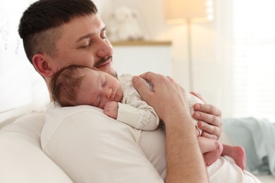 Photo of Father with his cute newborn baby on sofa indoors