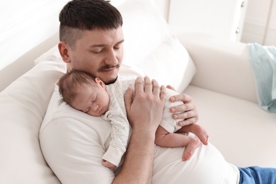 Photo of Father with his cute newborn baby on sofa indoors