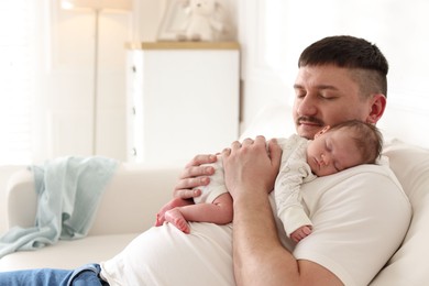 Photo of Father with his cute newborn baby on sofa indoors, space for text