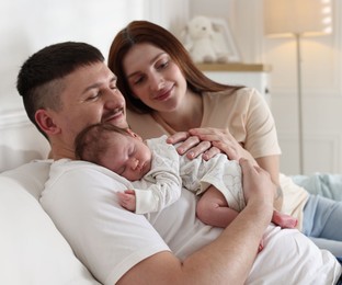 Photo of Happy parents with their cute newborn baby on sofa indoors